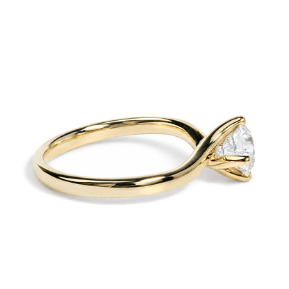 Close-up image of a yellow metal ring with a prong-set round white gemstone, shown from a side angle.