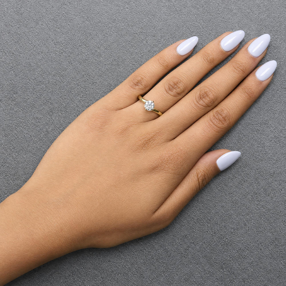 Yellow ring with a single round white gemstone in prong setting, shown worn on a model's hand, angled from above.