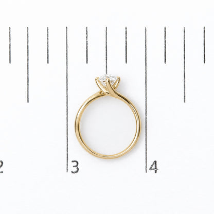 Close-up front view of a yellow metal ring with a single round white gemstone in a prong setting, shown on a measurement scale background.