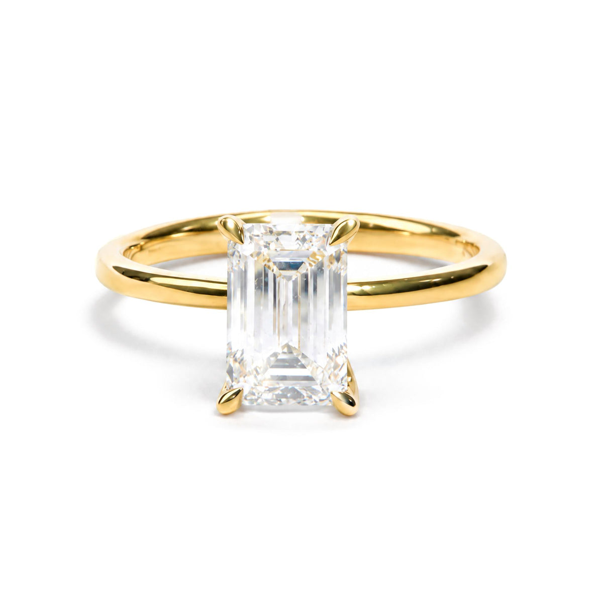 Close-up front angle of a yellow metal ring featuring a large emerald-shaped white gemstone in prong setting, accented by smaller round white gemstones in prong settings.