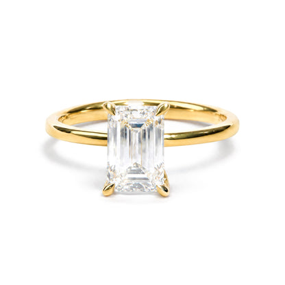 Close-up front angle of a yellow metal ring featuring a large emerald-shaped white gemstone in prong setting, accented by smaller round white gemstones in prong settings.