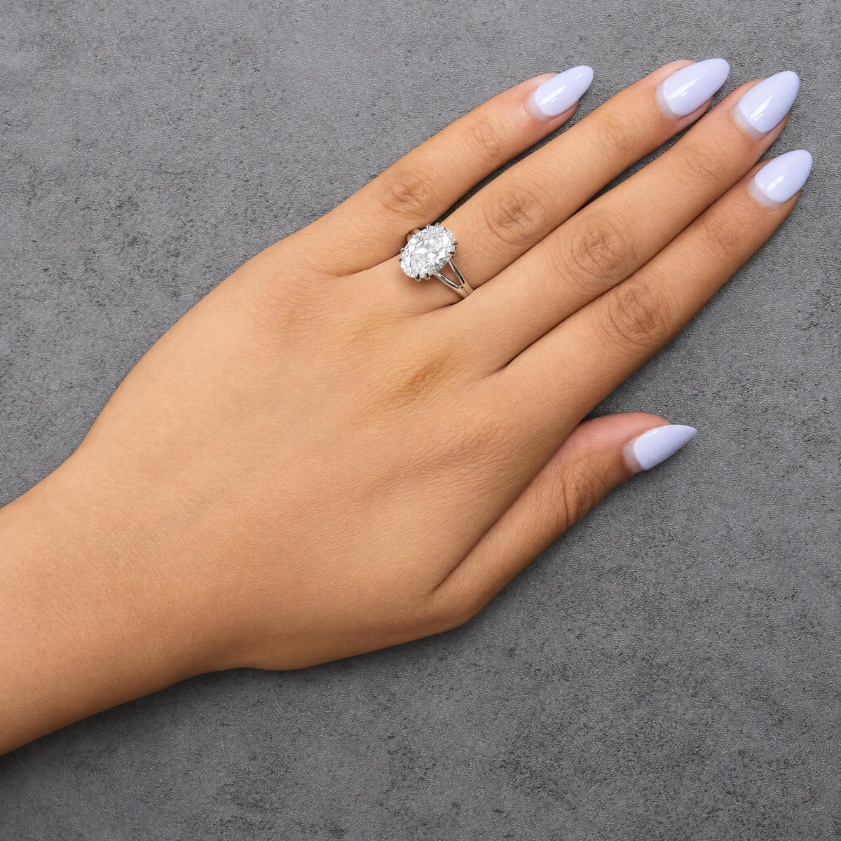 White metal ring with an oval-shaped white gemstone in a double claw prong setting, shown worn on a model's hand from a top angle.