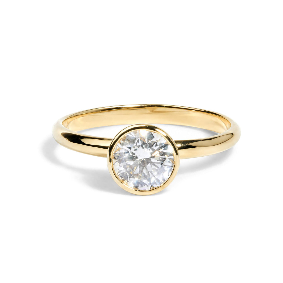 Close-up front angle of a yellow metal ring with a single round white gemstone in a bezel setting.
