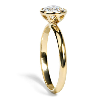 Close-up front angle of a yellow metal ring featuring a single white emerald-shaped gemstone in a bezel setting with openwork design around the setting.