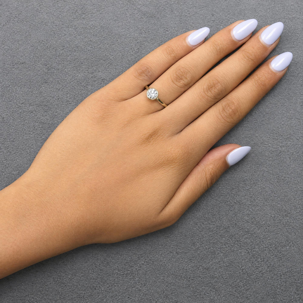 Yellow metal ring with a single white gemstone in a bezel setting, shown worn on a model's hand from a top angle.