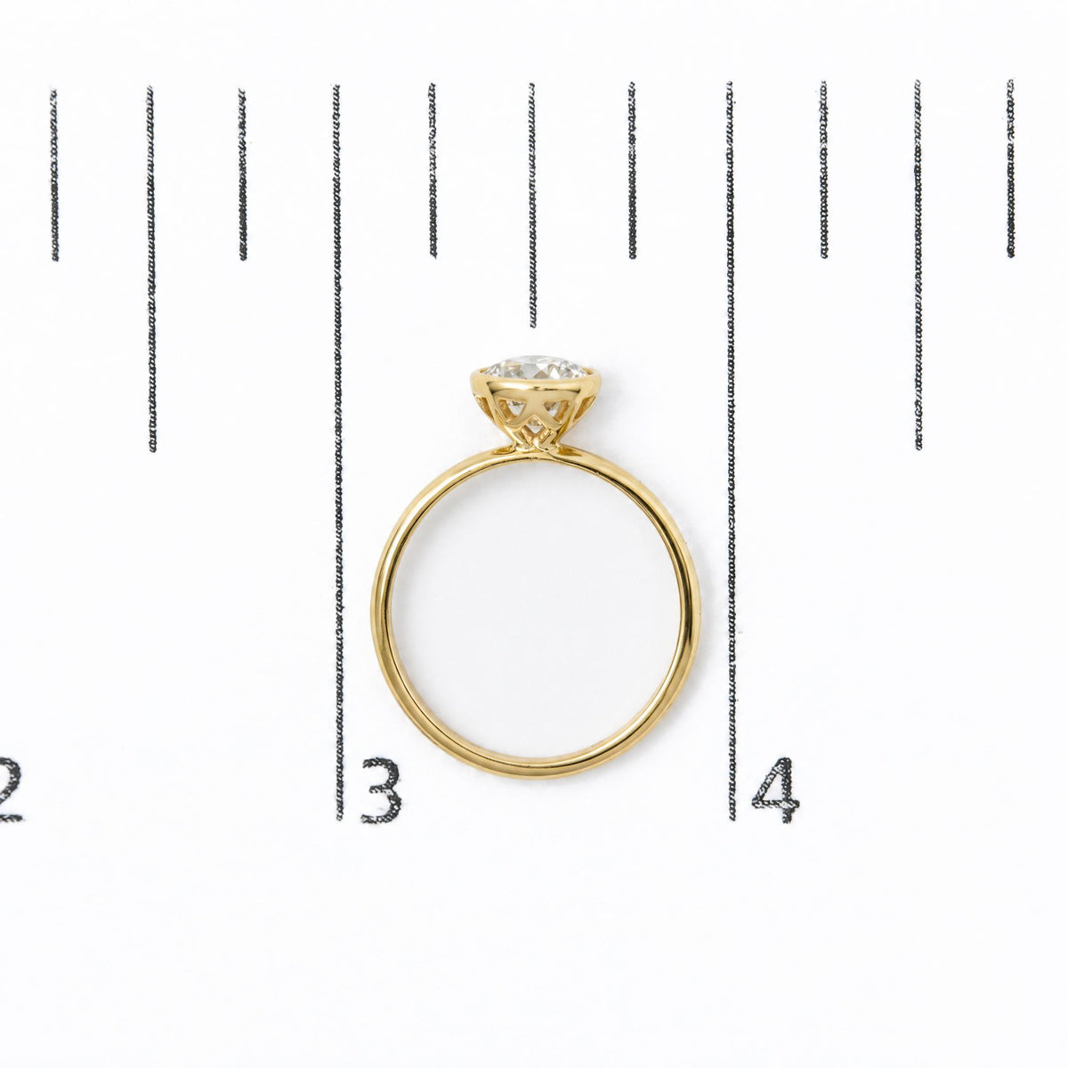 Yellow ring with a white emerald-shaped gemstone in a bezel setting, shown from a top-down angle on a size scale.