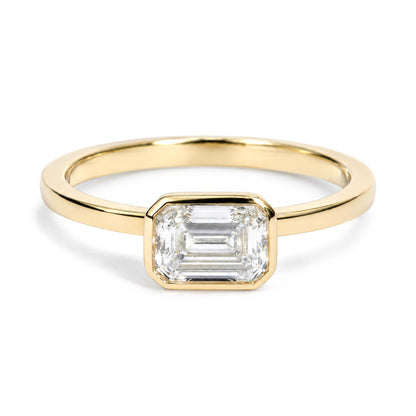 Close-up front view of a yellow metal ring featuring one white emerald-shaped gemstone in a bezel setting.