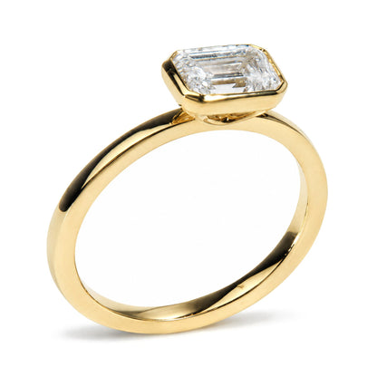 Close-up side angle of a yellow metal ring with a single white gemstone in an emerald shape bezel setting.