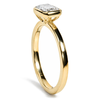 Close-up side angle of a yellow ring with an emerald-shaped white gemstone in a bezel setting.
