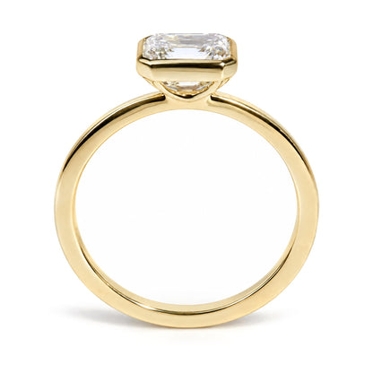 Close-up front angle of a yellow metal ring featuring a single emerald-shaped white gemstone in a bezel setting.