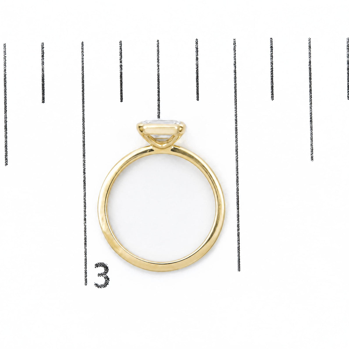 Yellow ring with a white emerald-shaped gemstone in a bezel setting, shown on a scale, top view.
