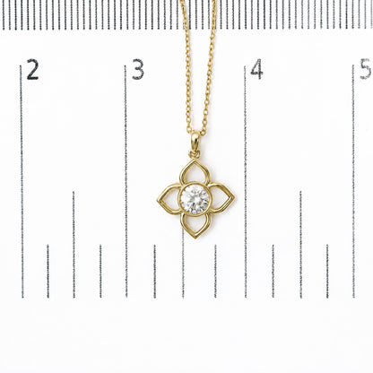 Close-up image of a yellow metal necklace pendant with a clover-shaped design, featuring a round white gemstone in a bezel setting, shown on a measurement scale from a top-down angle.