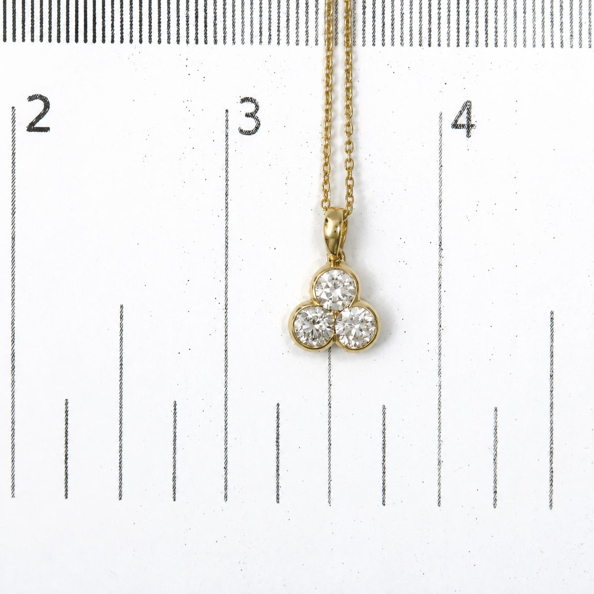 Close-up front view of a yellow metal necklace with a pendant featuring three round white gemstones in bezel settings, shown on a scale.