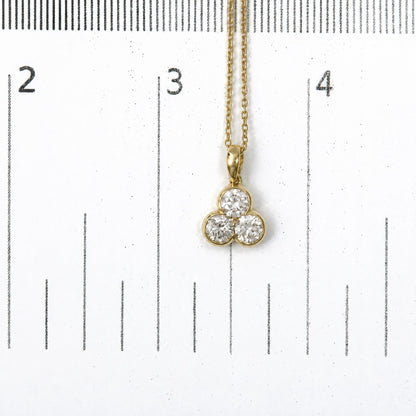 Close-up front view of a yellow metal necklace with a pendant featuring three round white gemstones in bezel settings, shown on a scale.