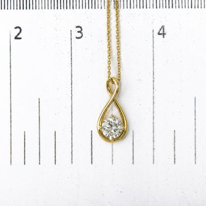 Close-up shot of a yellow metal necklace with an infinity-shaped pendant featuring a round white gemstone in a 4-prong setting, shown on a scale.