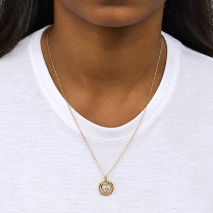 Close-up front view of a model wearing a yellow metal necklace with a round bezel-set white gemstone pendant in a heart-shaped design.