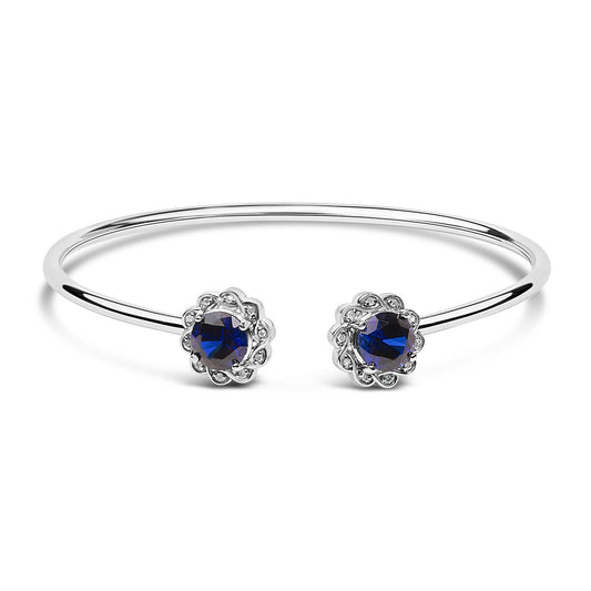 White open bangle bracelet with round blue gemstones and small white gemstones in prong settings, shown from a front angle on a white background.