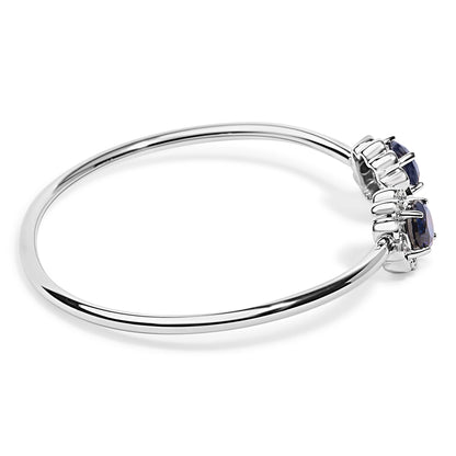 White metal bracelet with two large blue gemstones flanked by multiple small white gemstones, shown on a white background from a side angle.