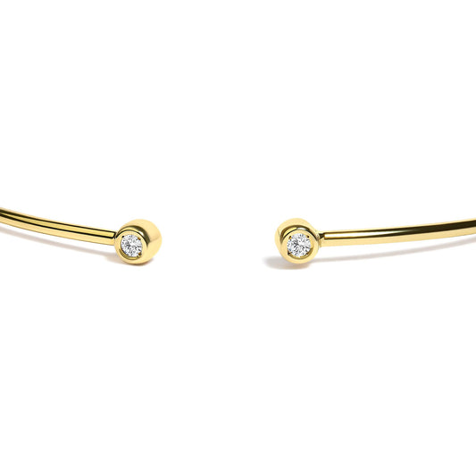 Close-up angled view of a yellow and white metal open bracelet with round white gemstones in bezel settings at each end.