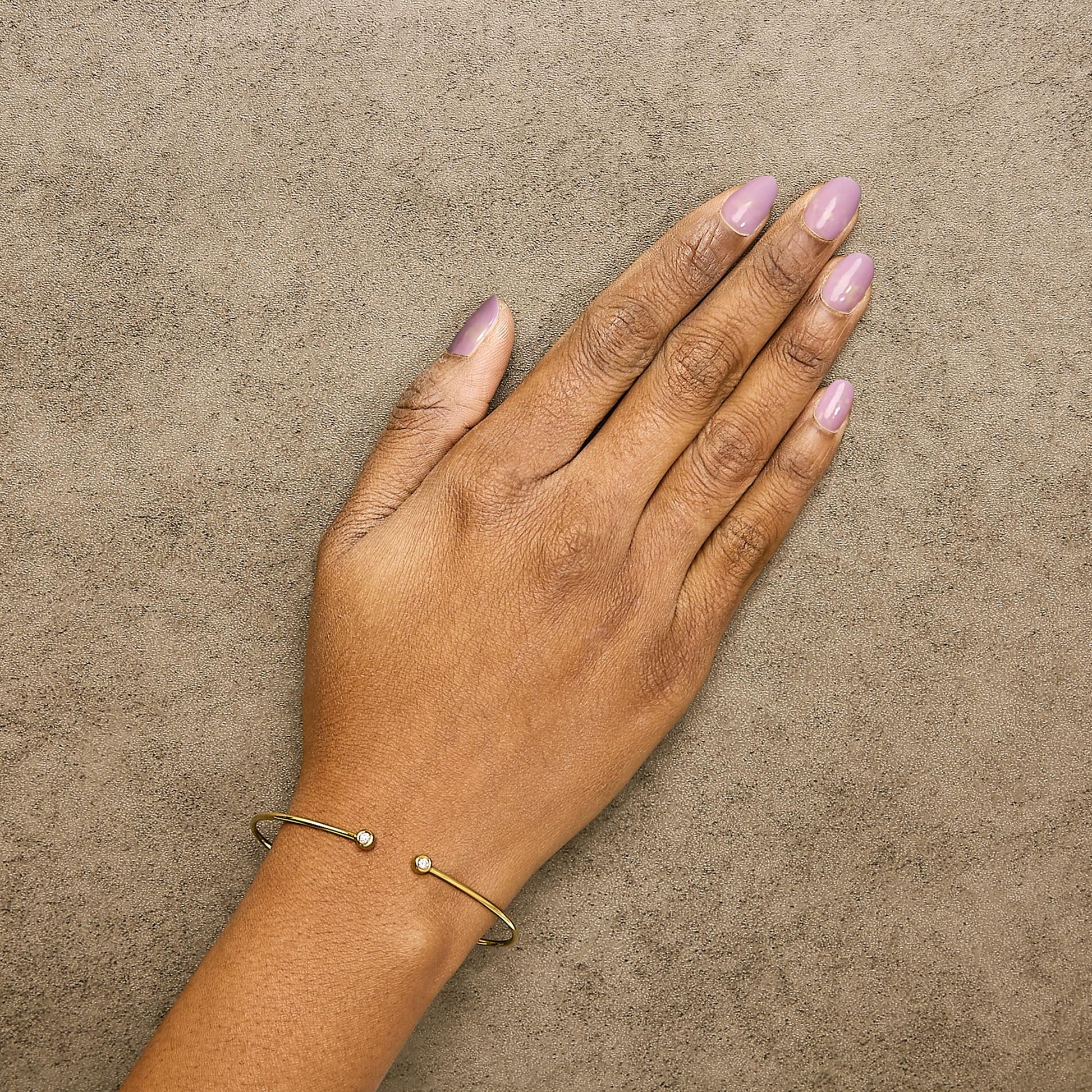 Close-up top view of a model's wrist wearing an open yellow and white metal bracelet with round white gemstones in bezel settings at each end.