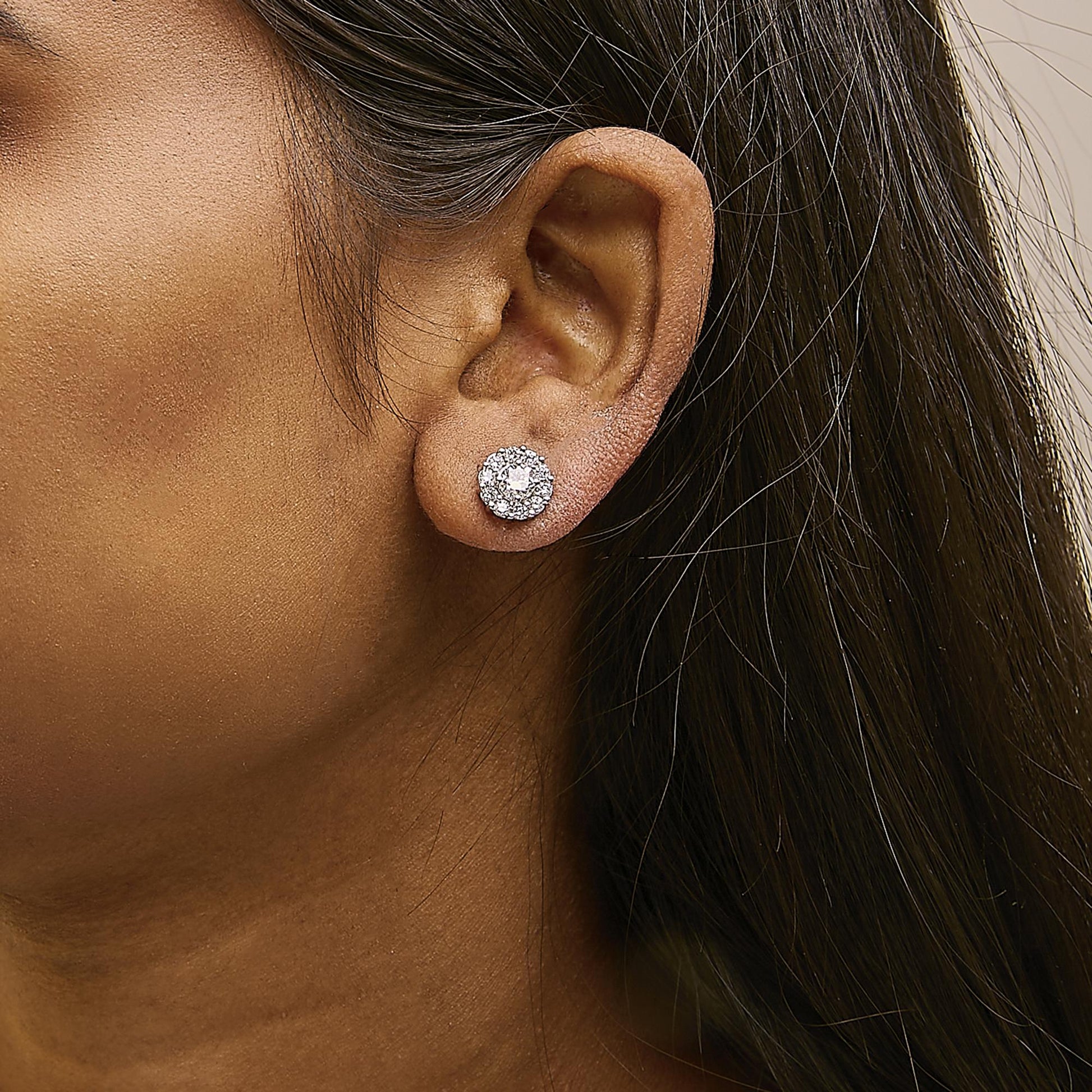 Close-up side view of a model wearing round white gemstone cluster stud earrings with a central gemstone in 4-prong setting surrounded by smaller gemstones in shared prong setting, all set in white metal.