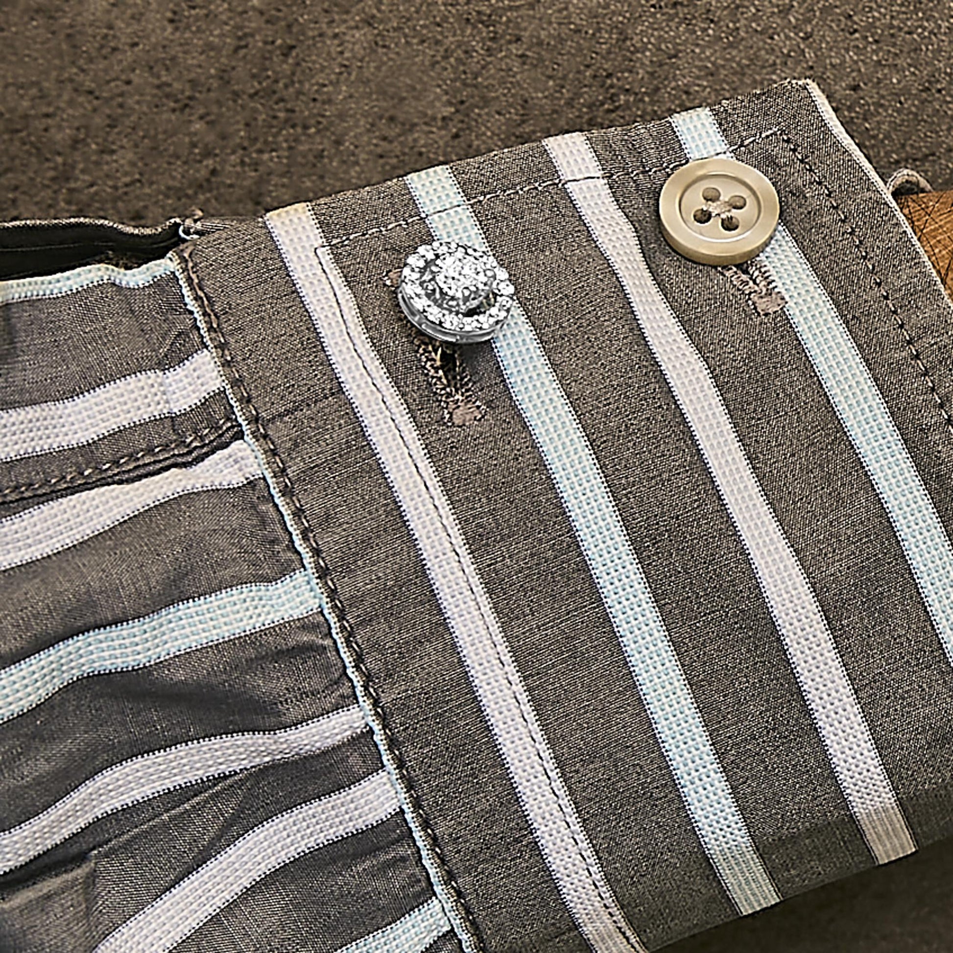Close-up angled view of a white metal cuff link adorned with round white gemstones in a 4-prong setting, worn on a striped fabric cuff with a beige button.