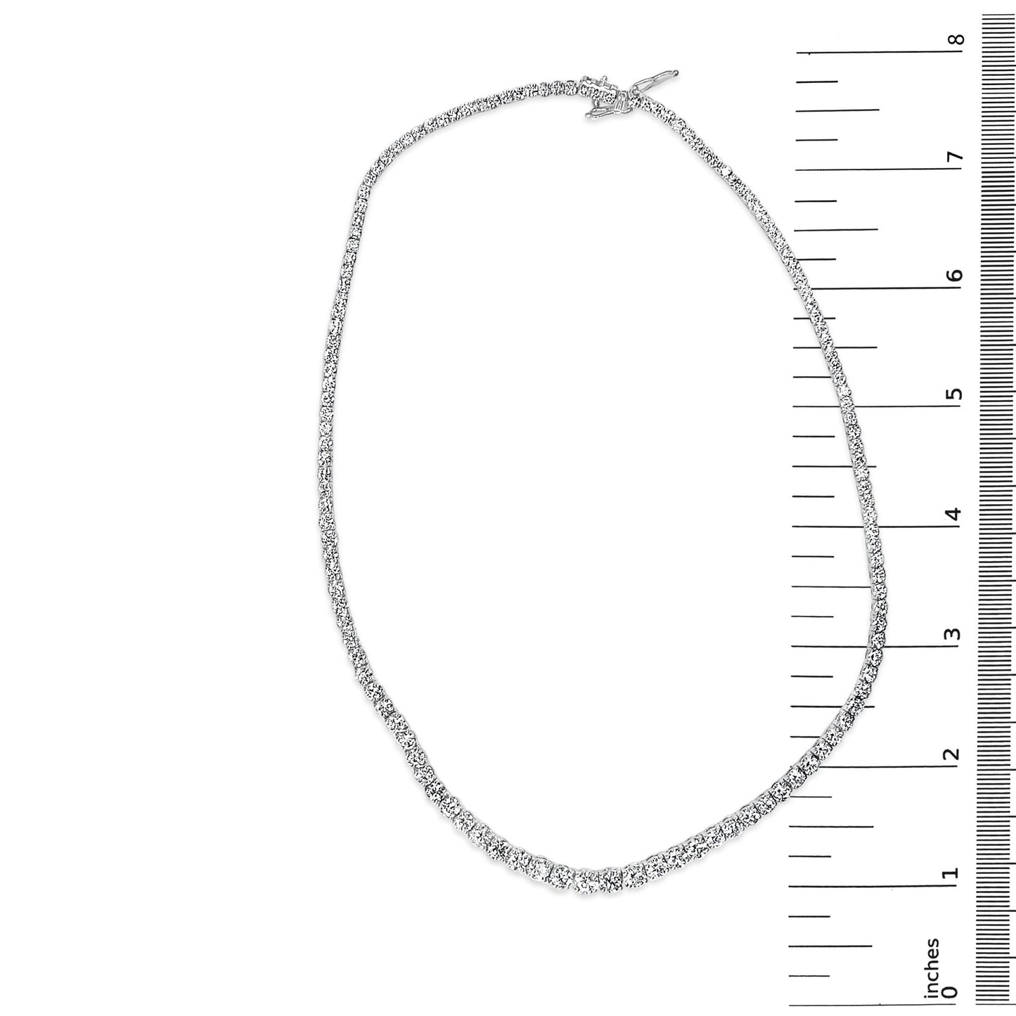 Top-down view of a white metal necklace with two sizes of round white gemstones in four-prong settings, placed on a ruler for size reference.