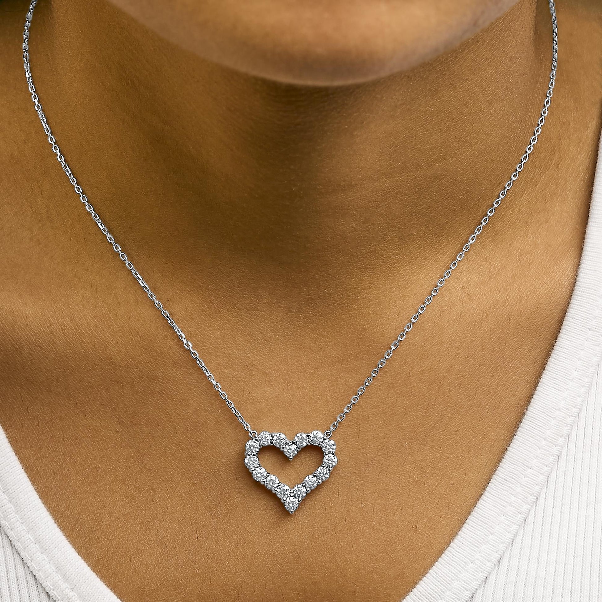 Close-up front view of a white heart-shaped necklace with round white gemstones in a shared prong setting shown worn on a model.