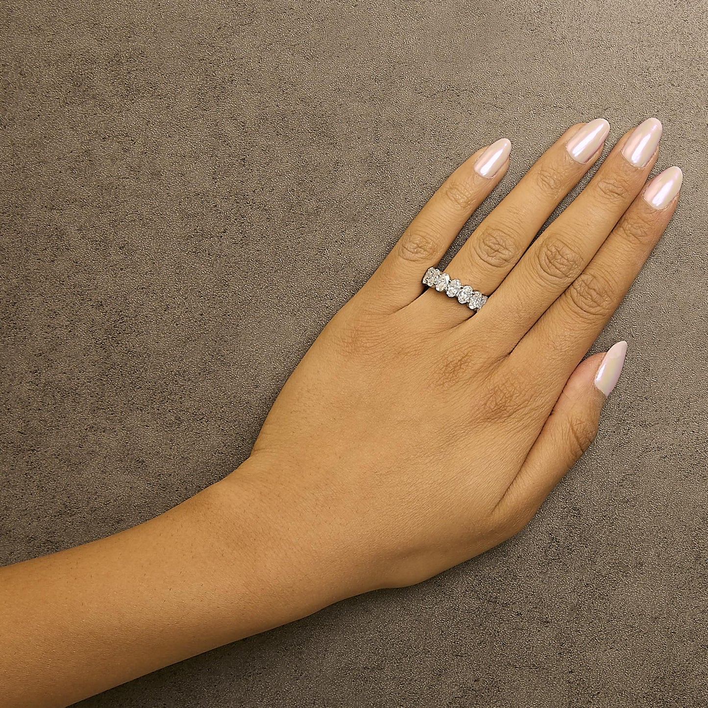 Close-up angled top view of a white metal ring with oval-shaped white gemstones in a shared prong setting, shown worn on a model's finger.