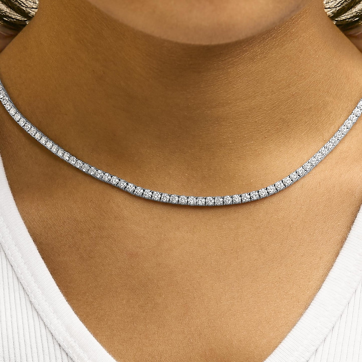 Close-up front view of a white necklace with round white gemstones in 4-prong settings, shown worn on a model.