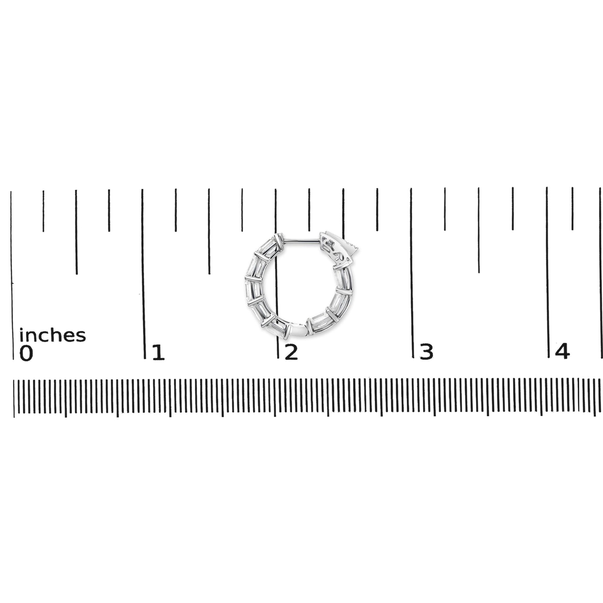 Close-up image of a white metal hoop earring with multiple emerald-shaped white gemstones in a shared prong setting, shown on a measurement scale.