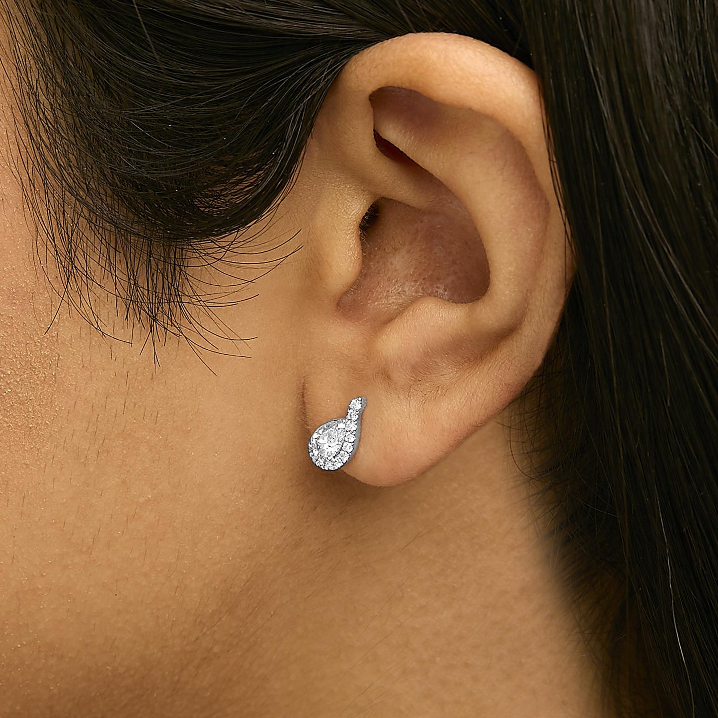 Close-up side view of a model wearing a white metal earring featuring a pear-shaped white gemstone surrounded by round white gemstones in a prong setting.