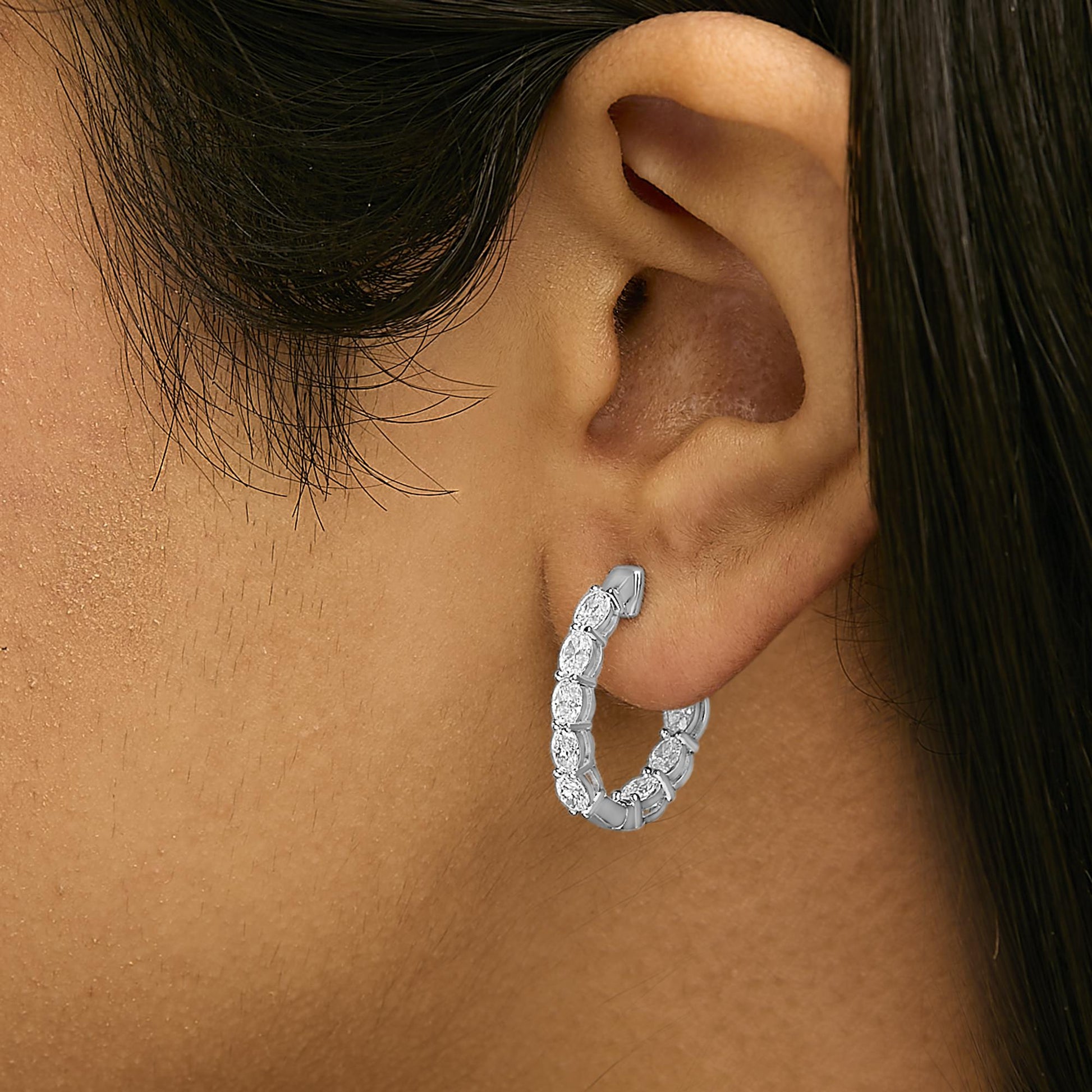 Close-up side view of a white metal hoop earring with multiple oval-shaped white gemstones in shared prong settings, shown worn on a model.