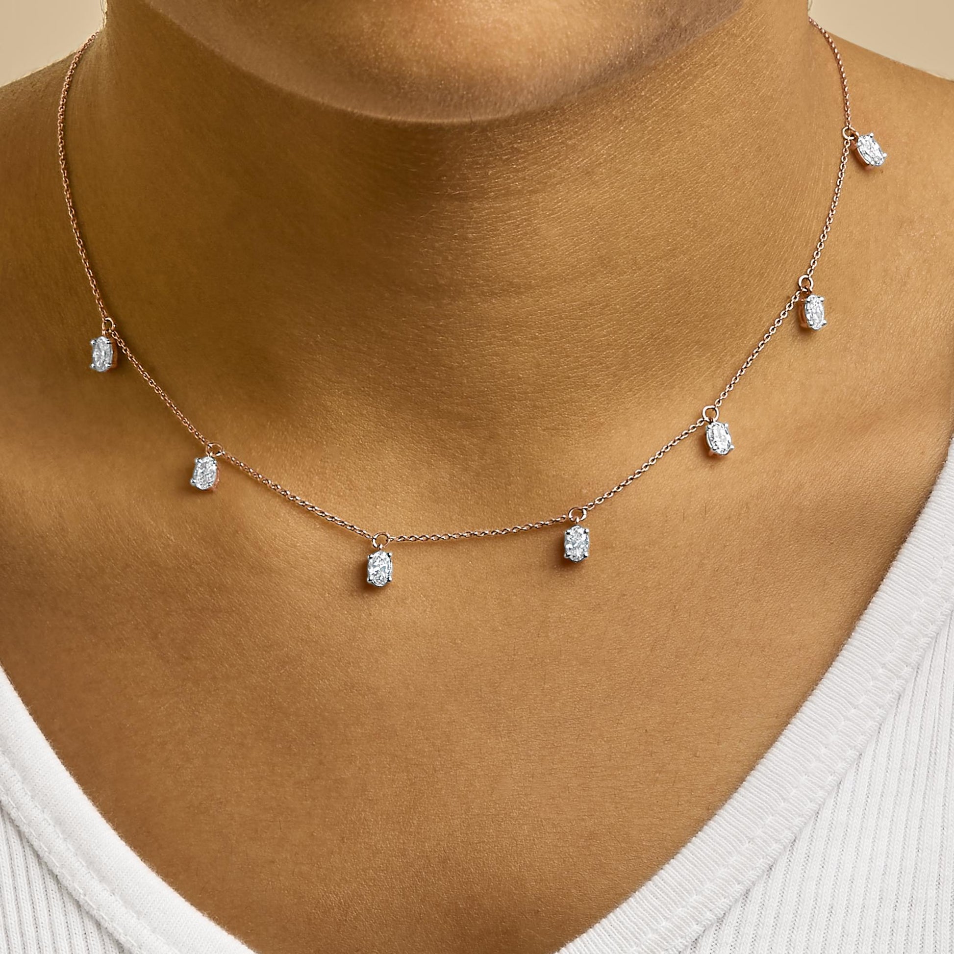 Close-up front view of a rose-colored necklace worn on a model's neck, featuring a delicate chain with multiple small oval-shaped white gemstones in 4-prong settings evenly spaced along the chain.