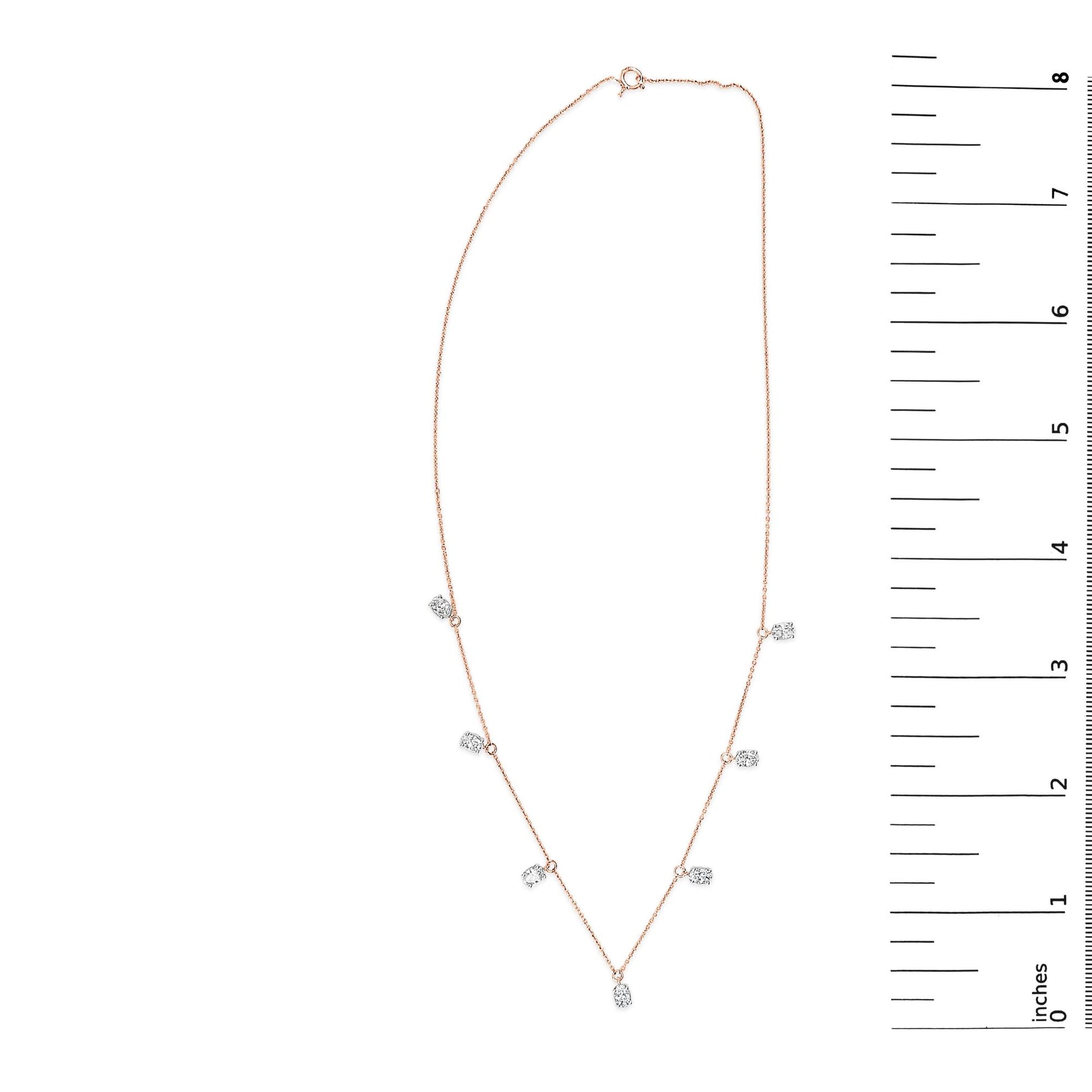 Rose-colored necklace with seven oval-shaped white gemstones in 4-prong settings, laid flat and shown next to a vertical scale.