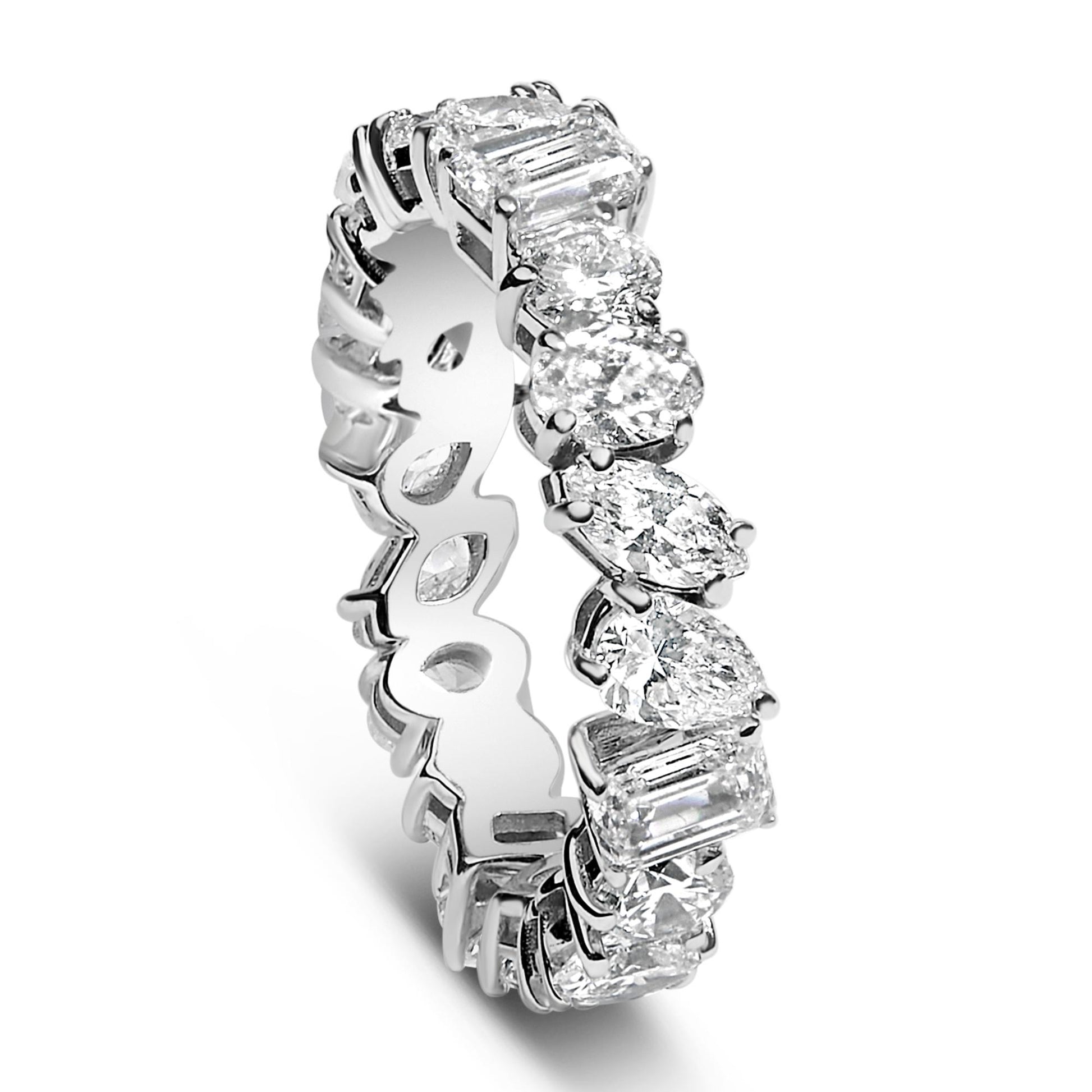 Close-up angled view of a white metal eternity ring featuring alternating round, oval, marquise, pear, and emerald-shaped white gemstones set in prongs around the band.