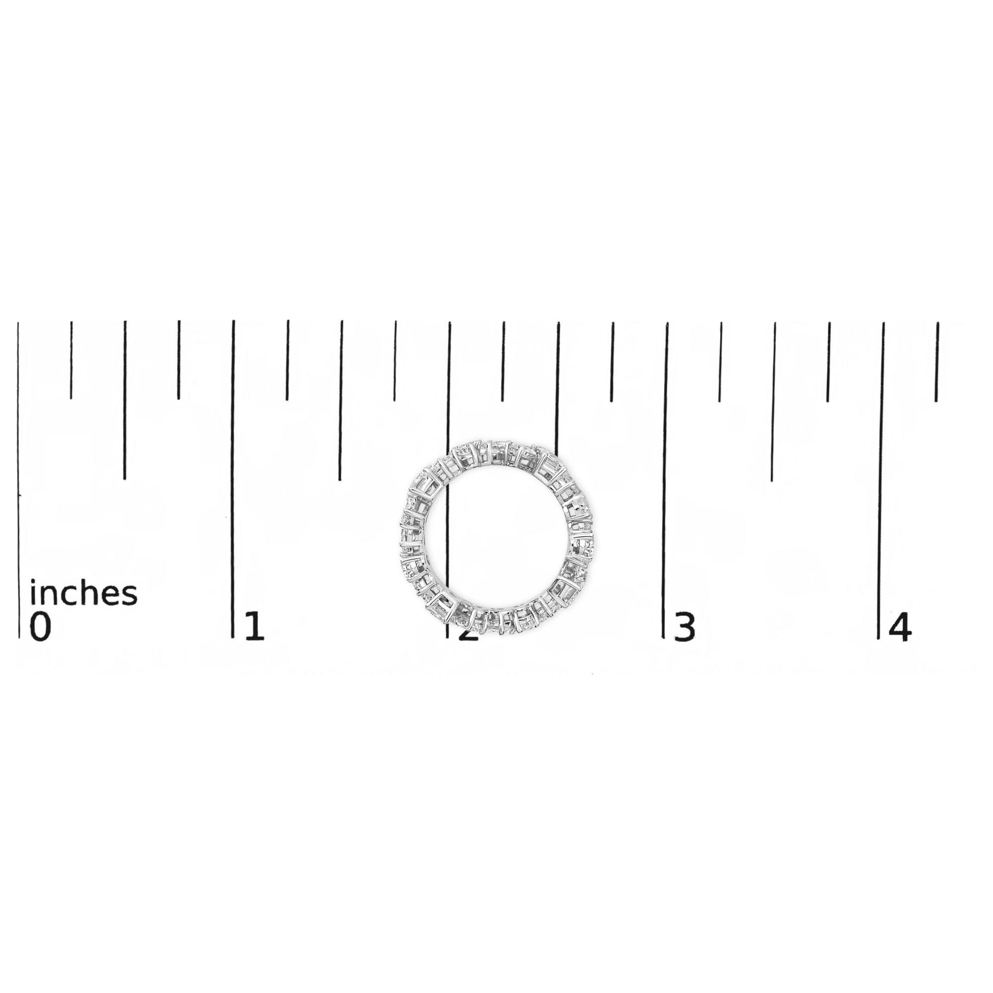 White metal ring with emerald-shaped gemstones in a continuous prong setting, shown from the top on a ruler scale.