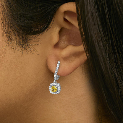 Close-up side view of a model wearing a white metal earring with a drop design, featuring a cushion-shaped yellow gemstone surrounded by small round white gemstones along the drop and around the central stone.