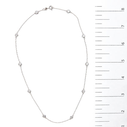 Close-up image of a white necklace with round bezel-set white gemstones evenly spaced along a thin chain, shown flat on a white surface next to a measurement scale.