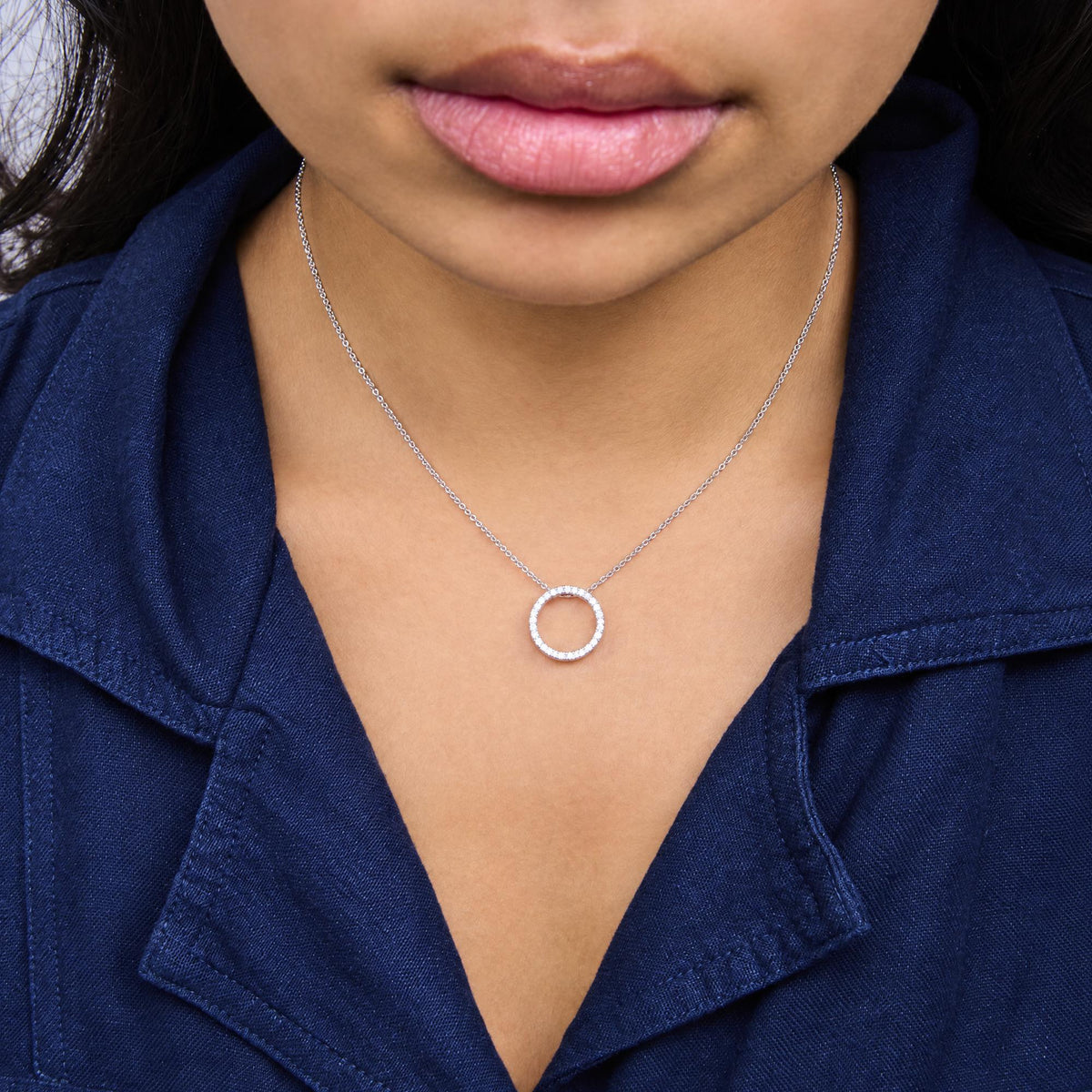 White metal necklace with a circular pendant encrusted with round white gemstones in prong settings, shown worn on a model, close-up front view.