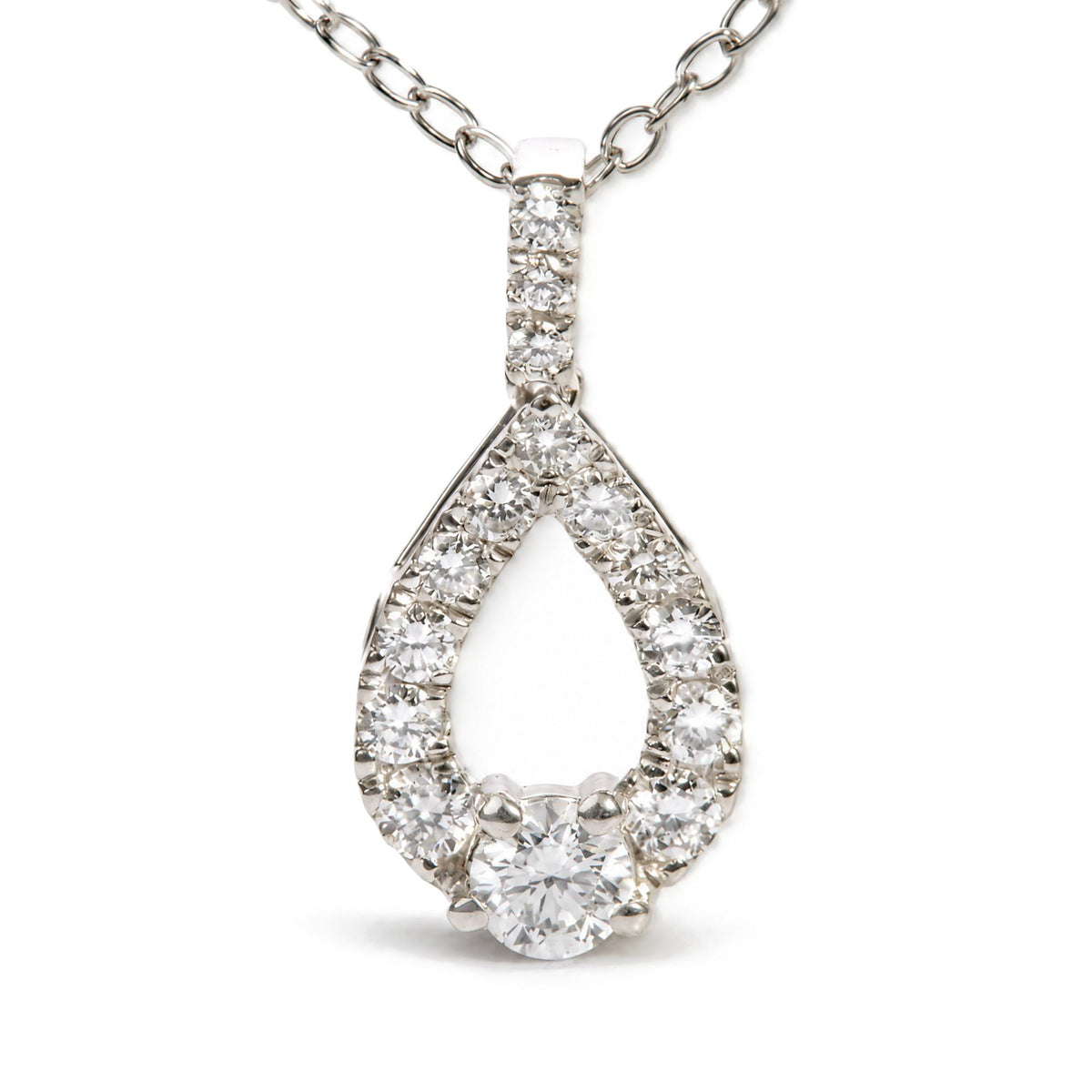 Close-up front angled shot of a white metal necklace pendant featuring a teardrop shape outlined with round white gemstones in prong settings and a larger round white gemstone at the bottom center, with a chain of oval links.