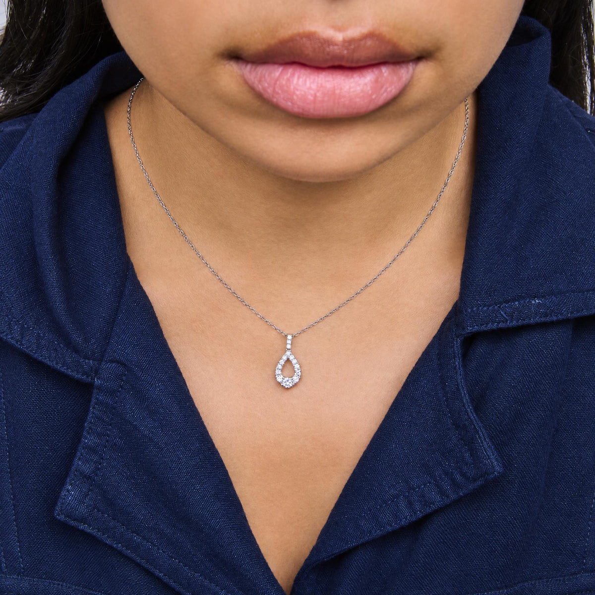 Close-up front view of a model wearing a white metal necklace with a pendant featuring multiple round white gemstones in a prong setting.