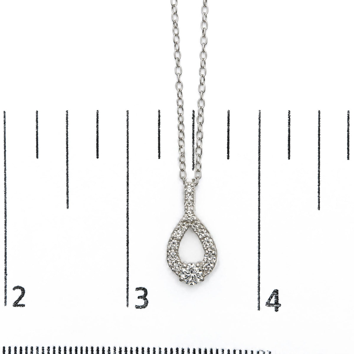 Close-up front view of a white necklace pendant with round white gemstones in a prong setting, shown on a scale.