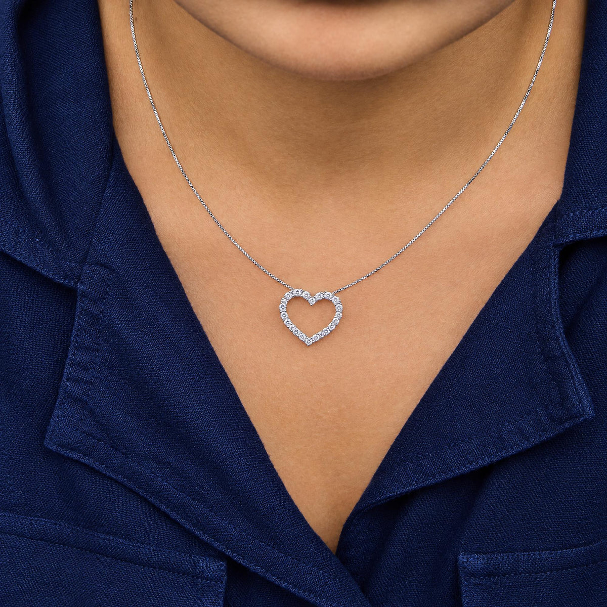 White metal necklace with a heart-shaped pendant featuring round white gemstones in prong settings, worn on a model, front close-up view.