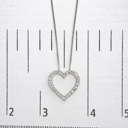Close-up front view of a white metal heart-shaped necklace pendant with round white gemstones in prong settings, shown on a measurement scale.