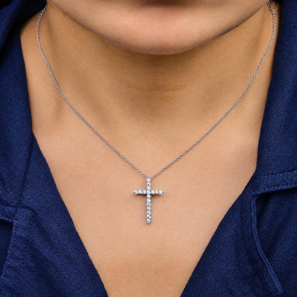 Close-up front view of a model wearing a white metal necklace with a cross-shaped pendant set with round white gemstones in a prong setting.