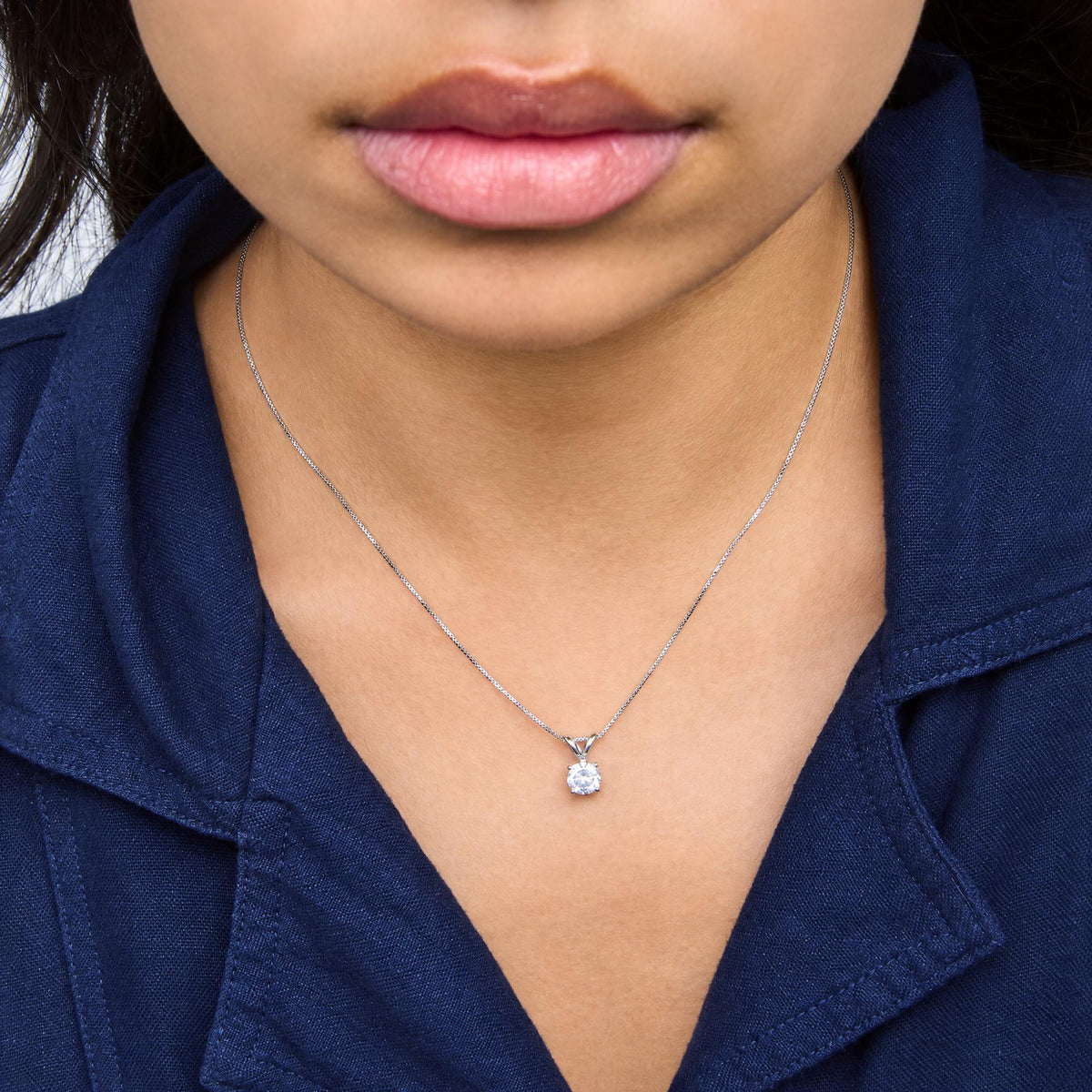 Close-up frontal view of a model wearing a white metal necklace with a single round white gemstone in a prong setting pendant.