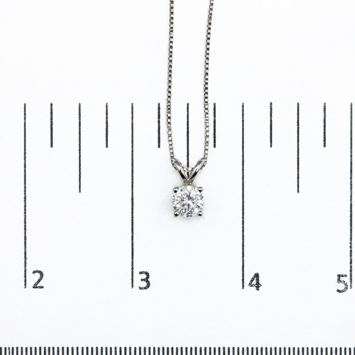 White metal necklace with a round white gemstone pendant in a prong setting, shown on a scale, top-down angle.