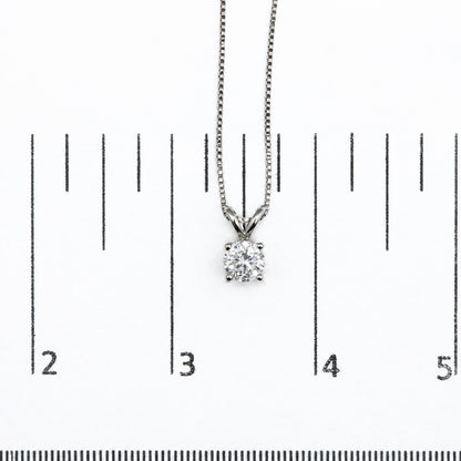 White metal necklace with a round white gemstone pendant in a prong setting, shown on a scale, top-down angle.