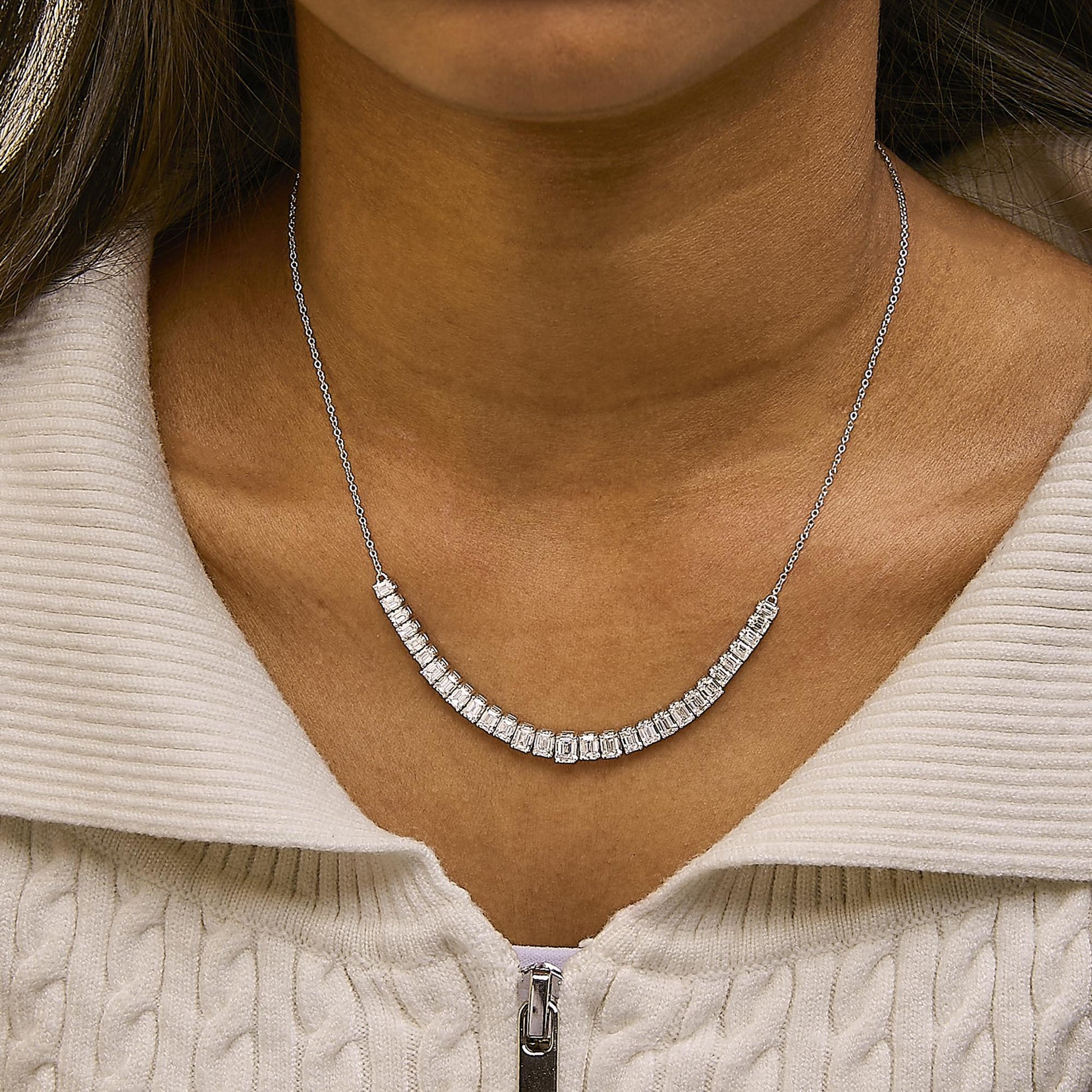 Necklace with a curved row of emerald-shaped white gemstones set in four-prong settings on a white metal chain, shown worn on a model, front-facing angle.